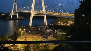 A cable-stayed bridge at dusk with illuminated cables and towers, overlooking a body of water and a parking area. - D Capstone (Batam)