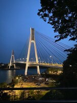 Un puente atirantado al anochecer con cables y torres iluminadas, con vista a un cuerpo de agua y un estacionamiento.