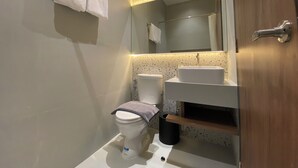 A modern bathroom with a toilet, sink, and mirror. - D Capstone (Batam)
