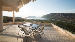 Una terraza con mesa y sillas, vista a un cuerpo de agua y colinas circundantes.