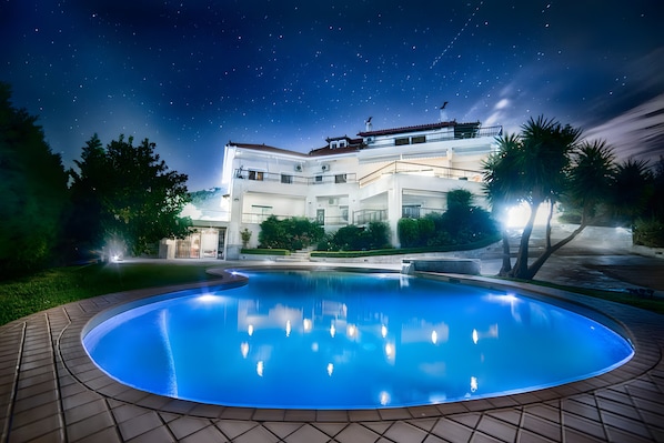A large, modern hotel with a swimming pool, multiple balconies, and a starry night sky.