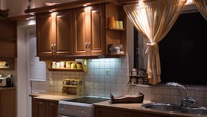 Una cocina con armarios de madera, estufa, pileta y ventana con cortinas.