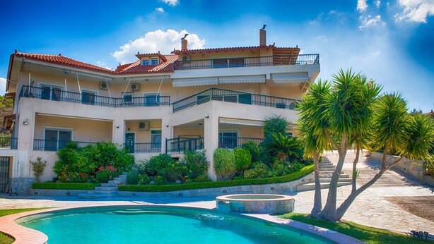 Un edificio de dos plantas con piscina, balcones y un jardín ajardinado.