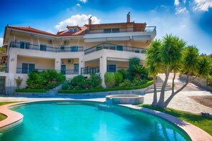 Un edificio de dos plantas con piscina, balcones y un jardín ajardinado.