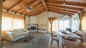 Un vaste salon doté d’un haut plafond en bois, d’une cheminée, d’un canapé, d’une table à manger avec des chaises et d’un coin cuisine.
