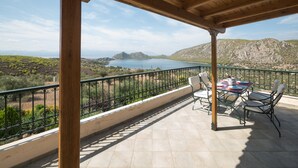 Une terrasse couverte, dotée d’une table et de chaises, qui offre une vue sur un paysage montagneux et une étendue d’eau.