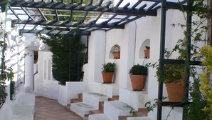 Un bâtiment blanc avec des marches en terre cuite menant à un espace couvert agrémenté d’une pergola.