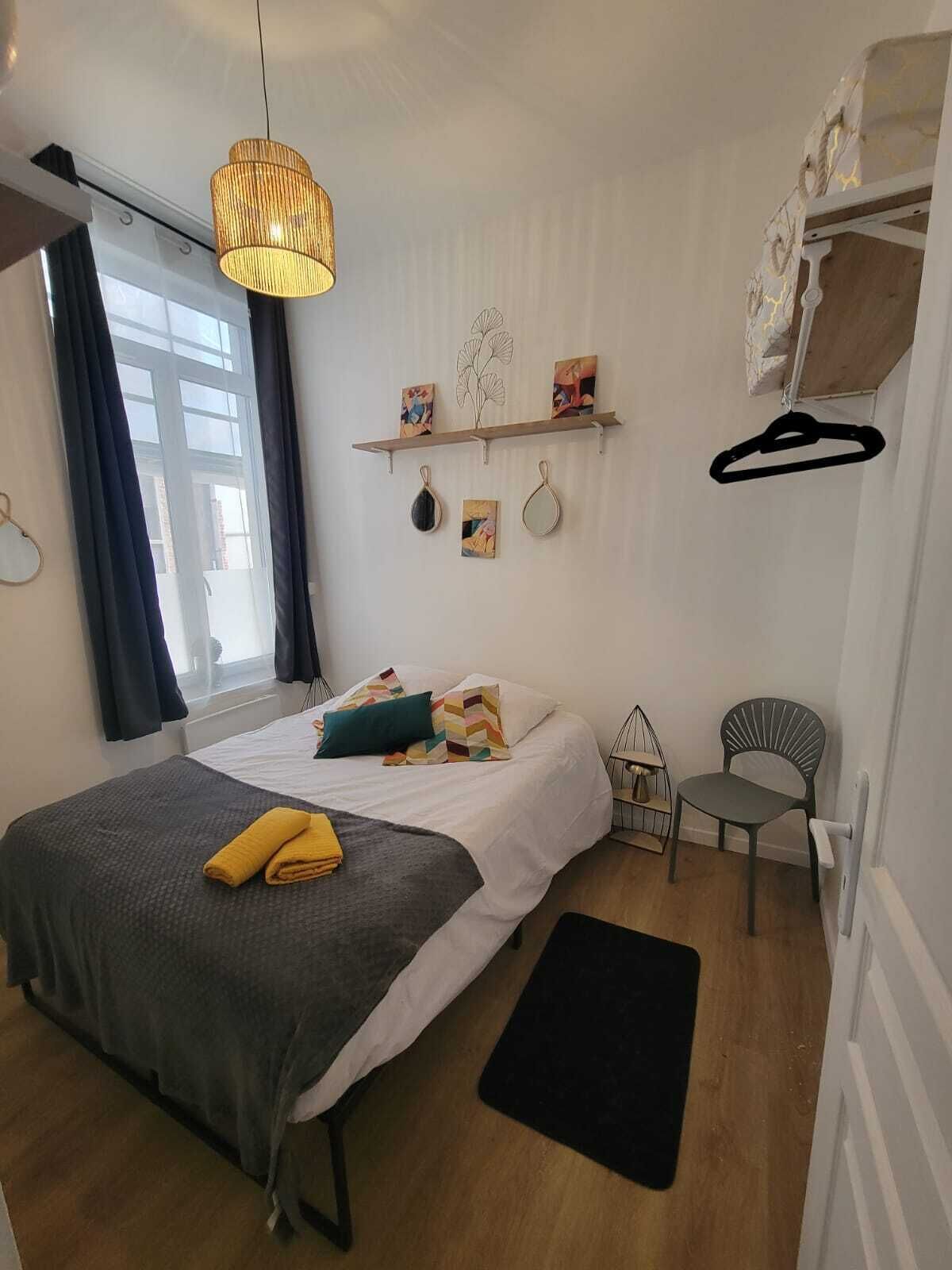 Een moderne slaapkamer met een bed, een hanglamp, een stoel en een plank met decoratieve objecten.