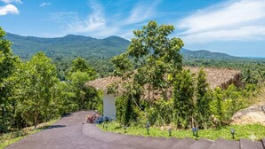 A rural setting with a thatched-roof building surrounded by lush greenery and mountains in the background. - Archies Paradise View (Ko Pha-ngan)
