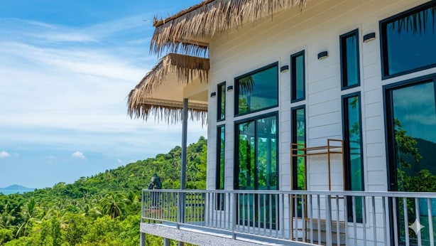 A modern building with large windows and a thatched roof, surrounded by lush greenery and a clear sky. - Archies Paradise View (Ko Pha-ngan)