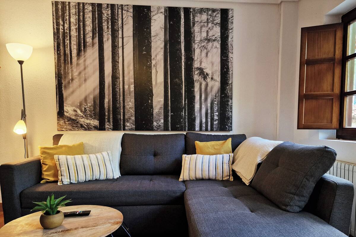A living room with a sectional sofa, a round coffee table, a floor lamp, and a large forest-themed wall art.