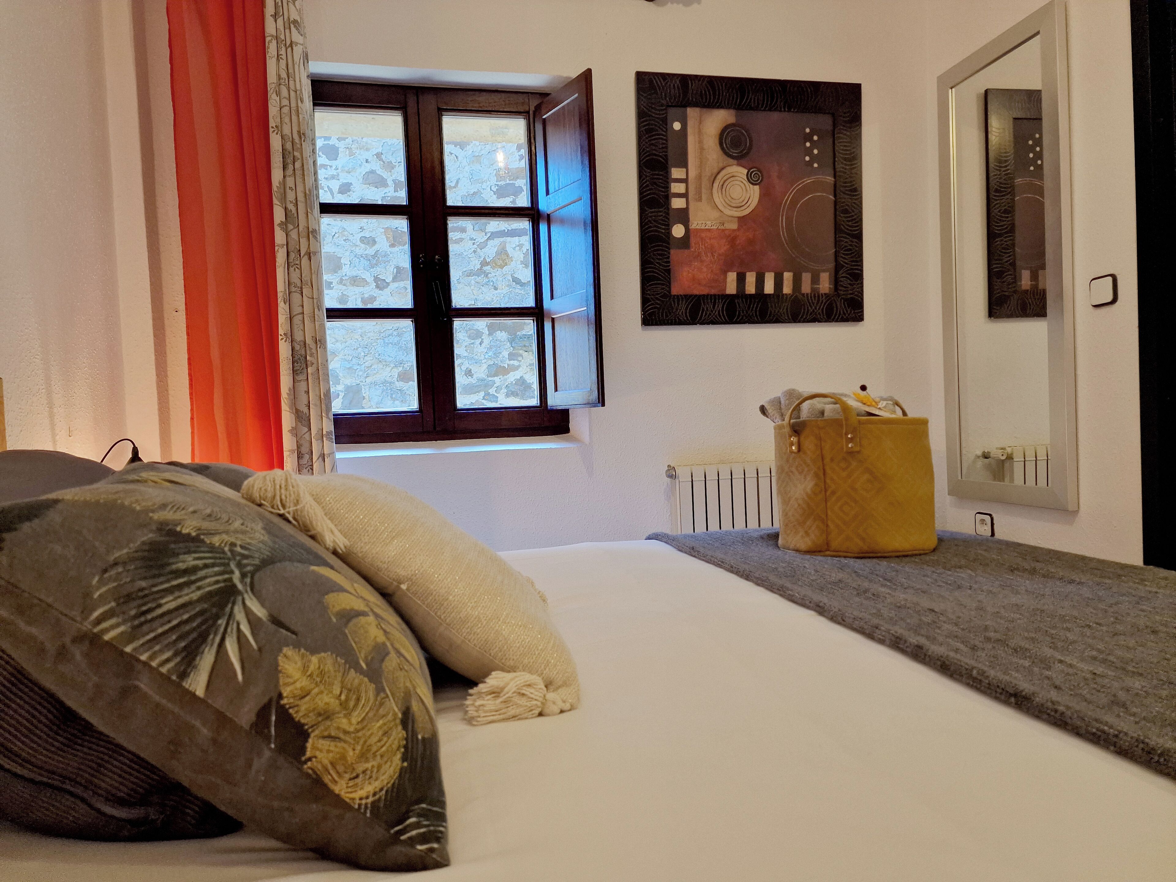 A bedroom with a bed, a window, a radiator, and a wall-mounted artwork.