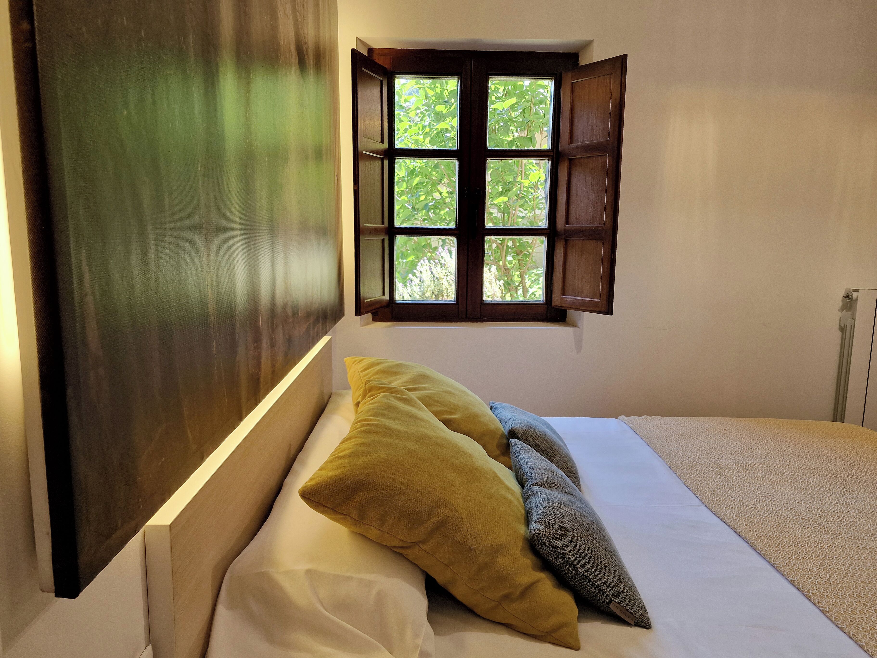 A room with a bed, a window with a view of greenery, and a radiator.