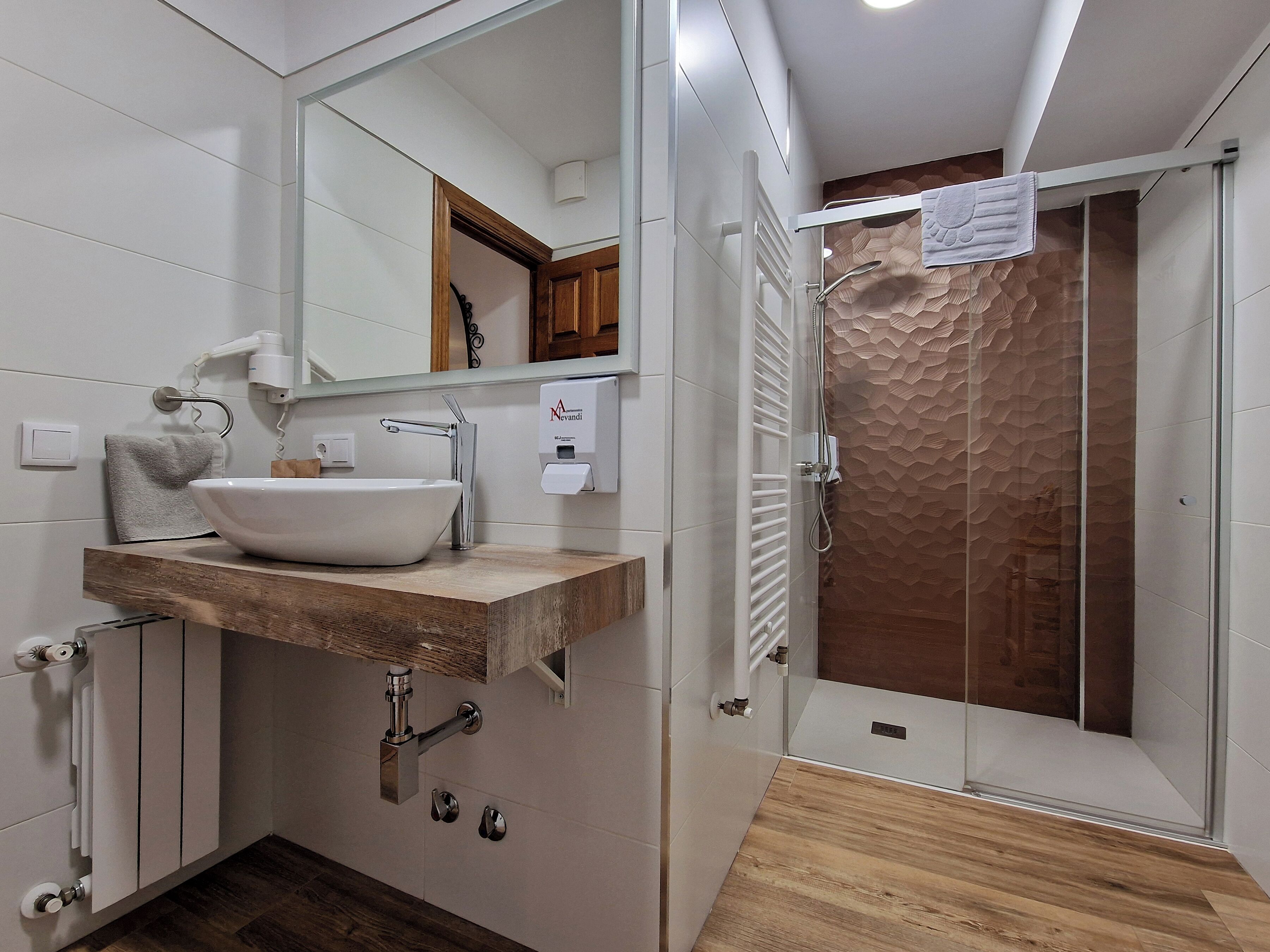 Un baño moderno con tocador de madera, un espejo grande, un lavamanos blanco y una ducha con pared texturizada.
