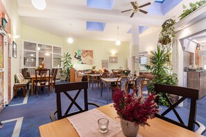 Un comedor con mesas, sillas, ventiladores de techo y plantas en macetas.
