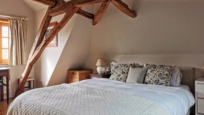 A bedroom with a large bed, wooden beams, a nightstand, a lamp, and a window with curtains. - The Farmhouse (MEYRONNE)