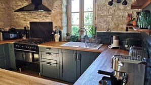 A rustic kitchen with a stone wall, wooden cabinets, a stove, a sink, and a coffee machine. - The Farmhouse (MEYRONNE)
