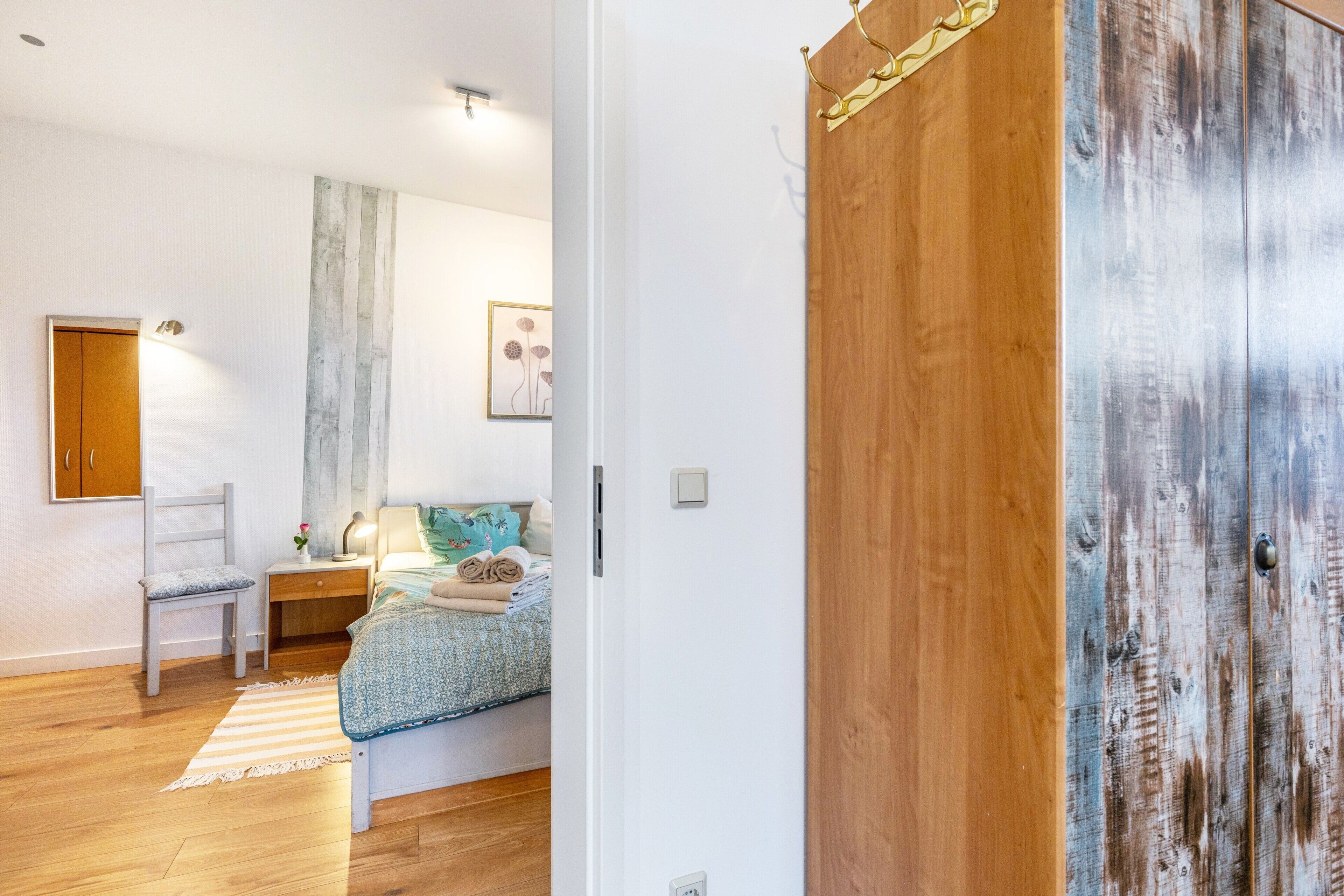 Quarto com cama, mesa de cabeceira, cadeira e porta de madeira.