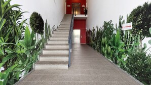 Un escalier avec un mur rouge, une pancarte indiquant «Aufzug» (ascenseur) et une main courante en métal.