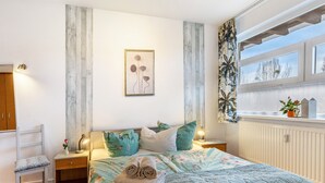 Une chambre à coucher comprenant un lit, des oreillers, une table de chevet, une chaise, une fenêtre avec vue et une œuvre d’art murale.