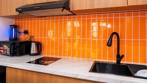 A kitchen with a microwave, toaster, and kettle on the counter, a black faucet, and orange-tiled backsplash. - Sóng and Sun Phu Quoc Hotel (Phu Quoc)