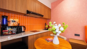 A kitchen with wooden cabinets, a microwave, a kettle, and a vase with flowers on a table. - Sóng and Sun Phu Quoc Hotel (Phu Quoc)