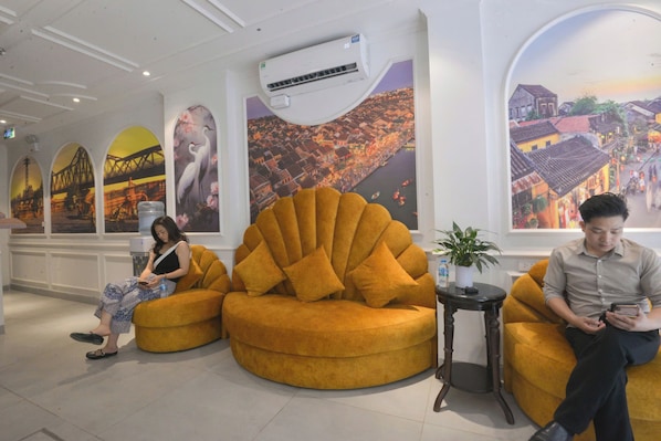 Un hall d’entrée doté d’un grand climatiseur, d’un canapé jaune, d’une petite table avec une plante et d’une fresque représentant un paysage urbain.