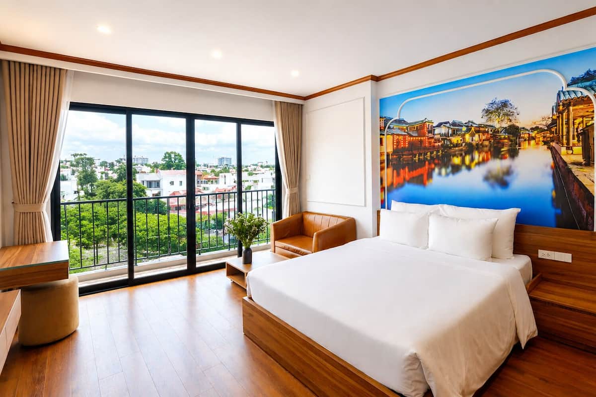 Hotelkamer met een groot bed, een bureau, een stoel en uitzicht op een stadsgezicht, evenals een muurschildering van een rivierlandschap.
