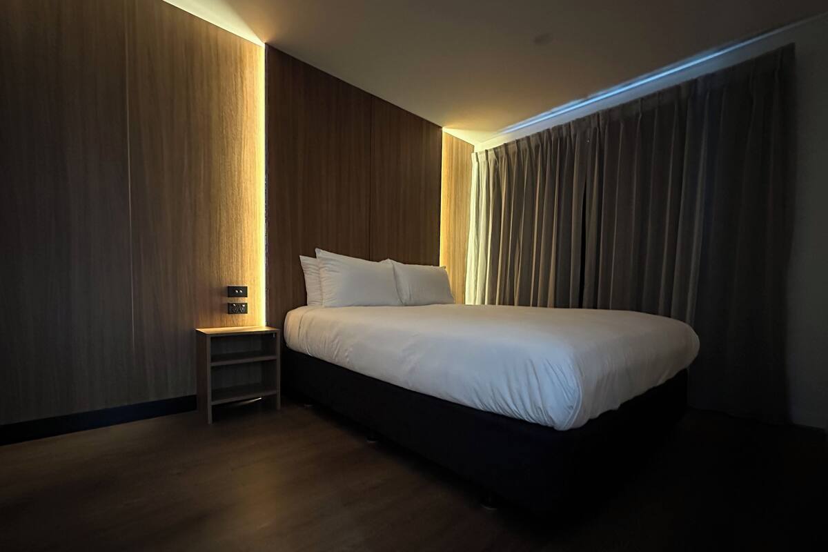 A modern hotel room with a large bed, a nightstand, and a wooden wall.