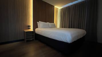 Ett modernt hotellrum med en stor säng, ett nattduksbord och en väggpanel av trä.