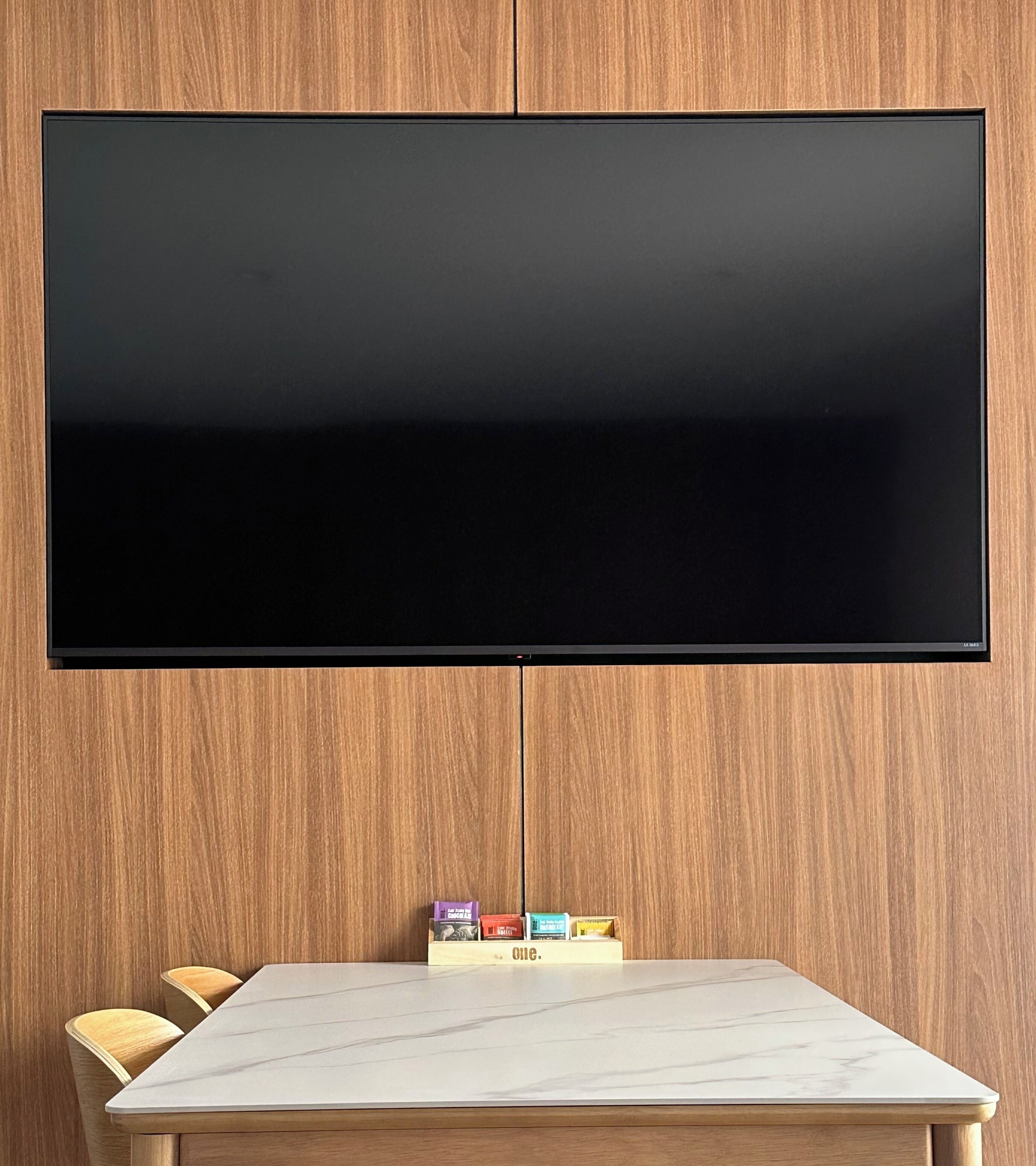 A flat-screen TV mounted on a wooden wall above a marble-topped table with chairs.