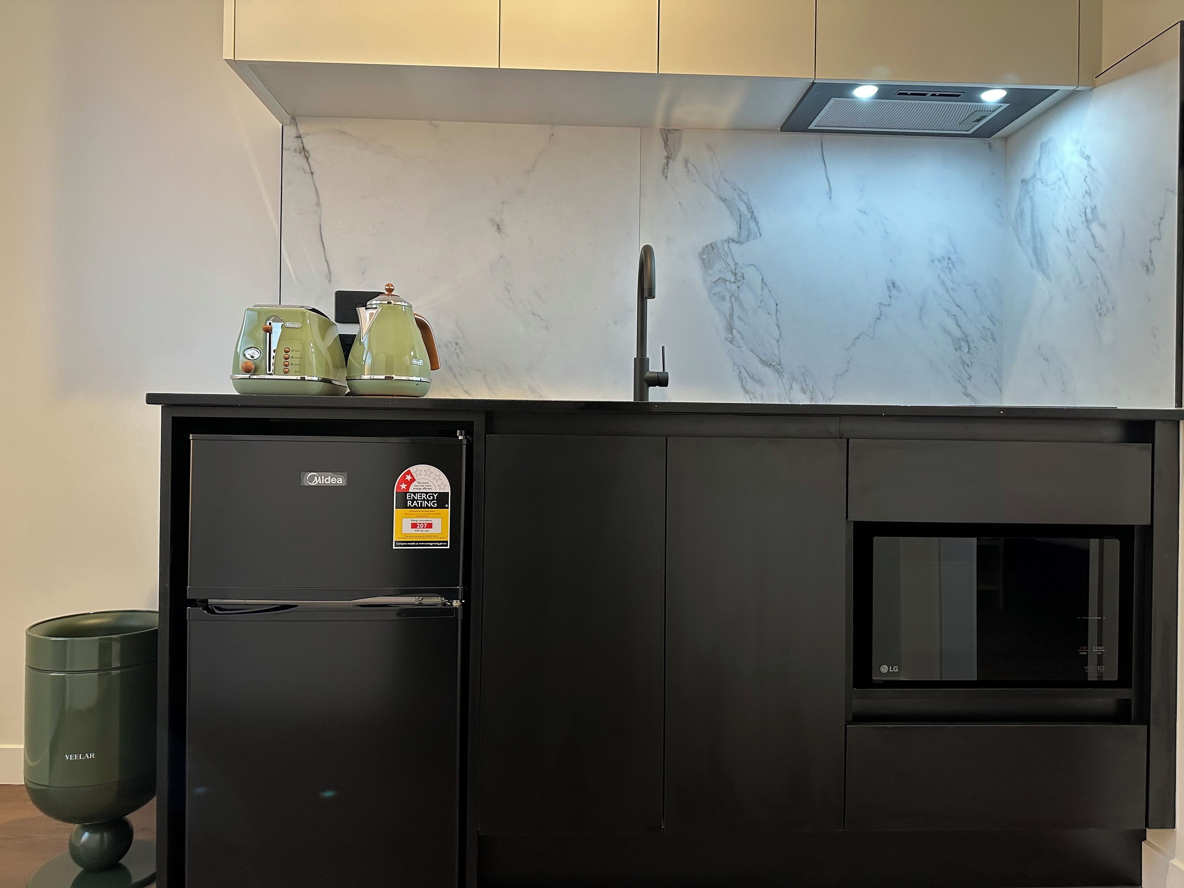 Una cocina moderna con un refrigerador negro, horno integrado y salpicadero de mármol.