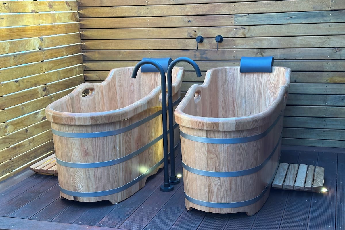 Two wooden tubs with metal bands, a wooden wall, and a metal faucet.