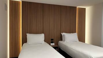 A hotel room with two single beds, wooden paneling on the walls, and a nightstand with a Wi-Fi sign.
