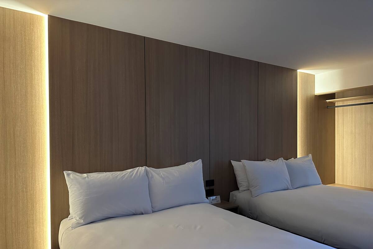 Two beds with white bedding in a hotel room with wooden panel walls and a visible 'WiFi' sign.