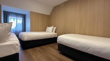 A hotel room with two single beds, a wooden floor, and a window with curtains.
