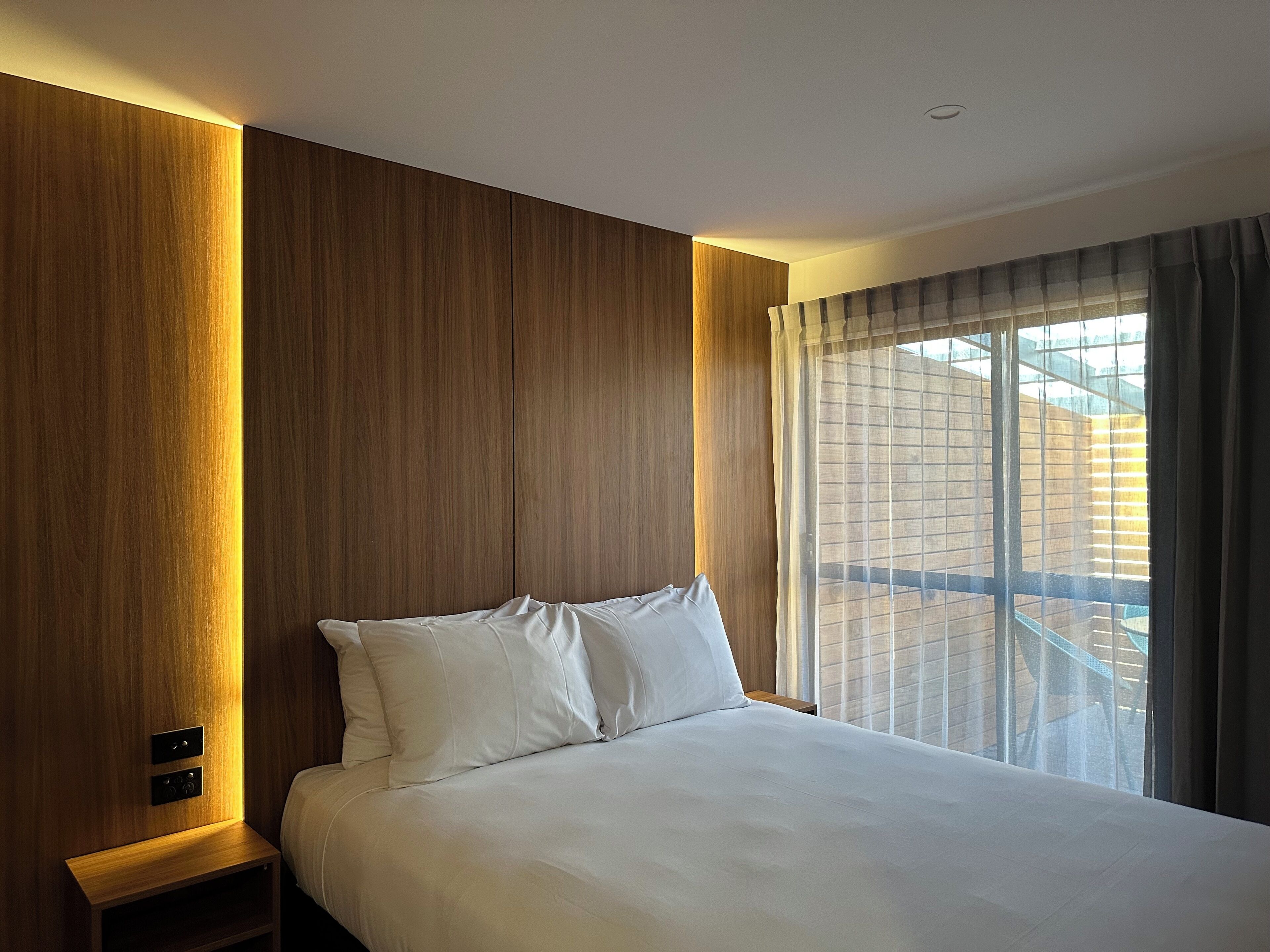 A hotel room with a large bed, wooden panel walls, a nightstand, and a window with curtains.