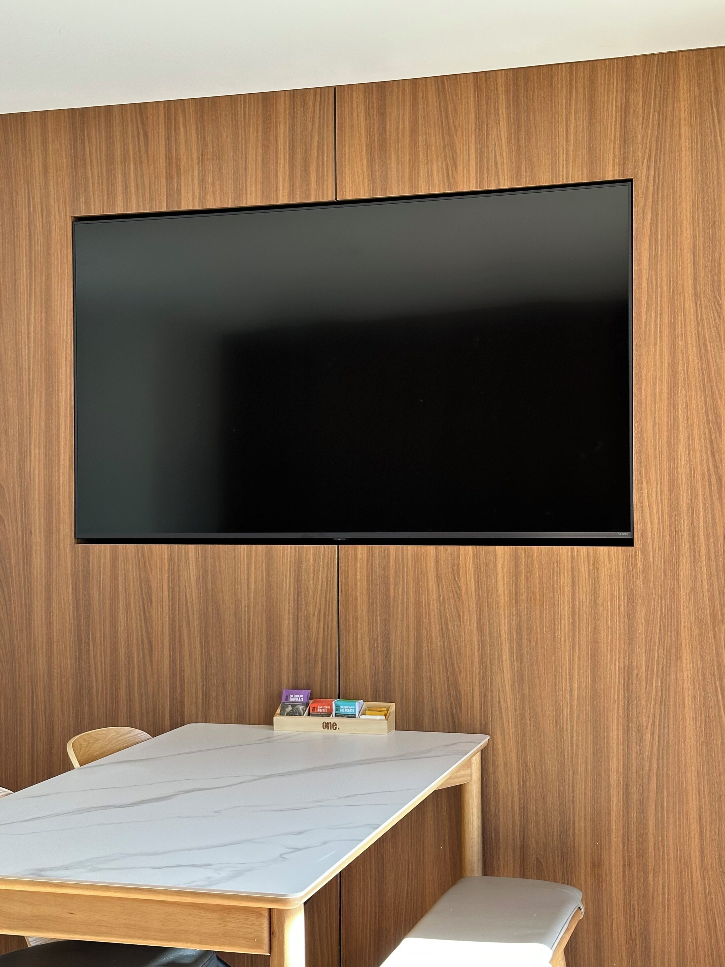 A modern room with a large flat-screen TV mounted on a wooden wall, a marble-topped table, and a bench.