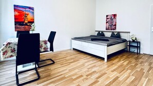 Ein modernes Schlafzimmer mit Holzboden, einem Bett mit grauer Bettwäsche, einem schwarzen Stuhl und zwei Wandbildern.