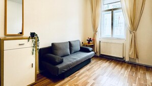 Ein modernes Wohnzimmer mit einem grauen Sofa, einer weißen Kommode und einem großen Fenster mit beigen Vorhängen.