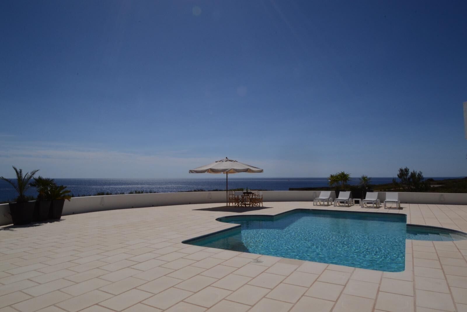 A rooftop pool with a clear view of the ocean, lounge chairs, and a table with an umbrella.