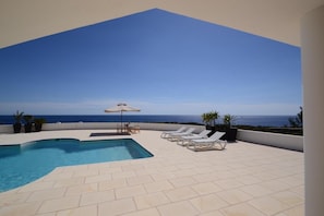 Una piscina en la azotea con sillones de descanso y vistas al océano.