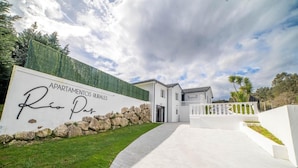 A modern building with a stone wall and a sign reading 'APARTAMENTOS RURALES Rio Pas.' - Rural Apartment Río Pas 1 (Oruña)