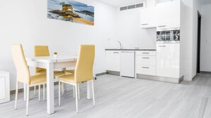 A modern kitchen with white cabinets, a dining table with yellow chairs, and a painting of a coastal scene. - Rural Apartment Río Pas 1 (Oruña)