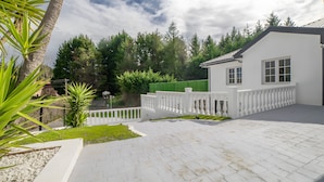 A white building with a paved driveway, a white fence, and a green fence in the background. - Rural Apartment Río Pas 1 (Oruña)