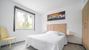 A bedroom with a bed, a chair, a window, and a painting on the wall. - Rural Apartment Río Pas 1 (Oruña)