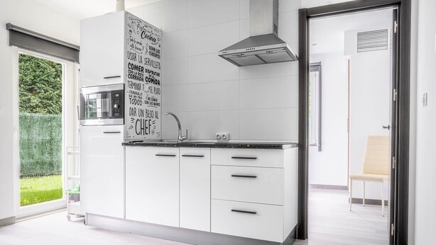 A modern kitchen with white cabinets, a stainless steel range hood, and a black countertop. - Rural Apartment Río Pas 1 (Oruña)