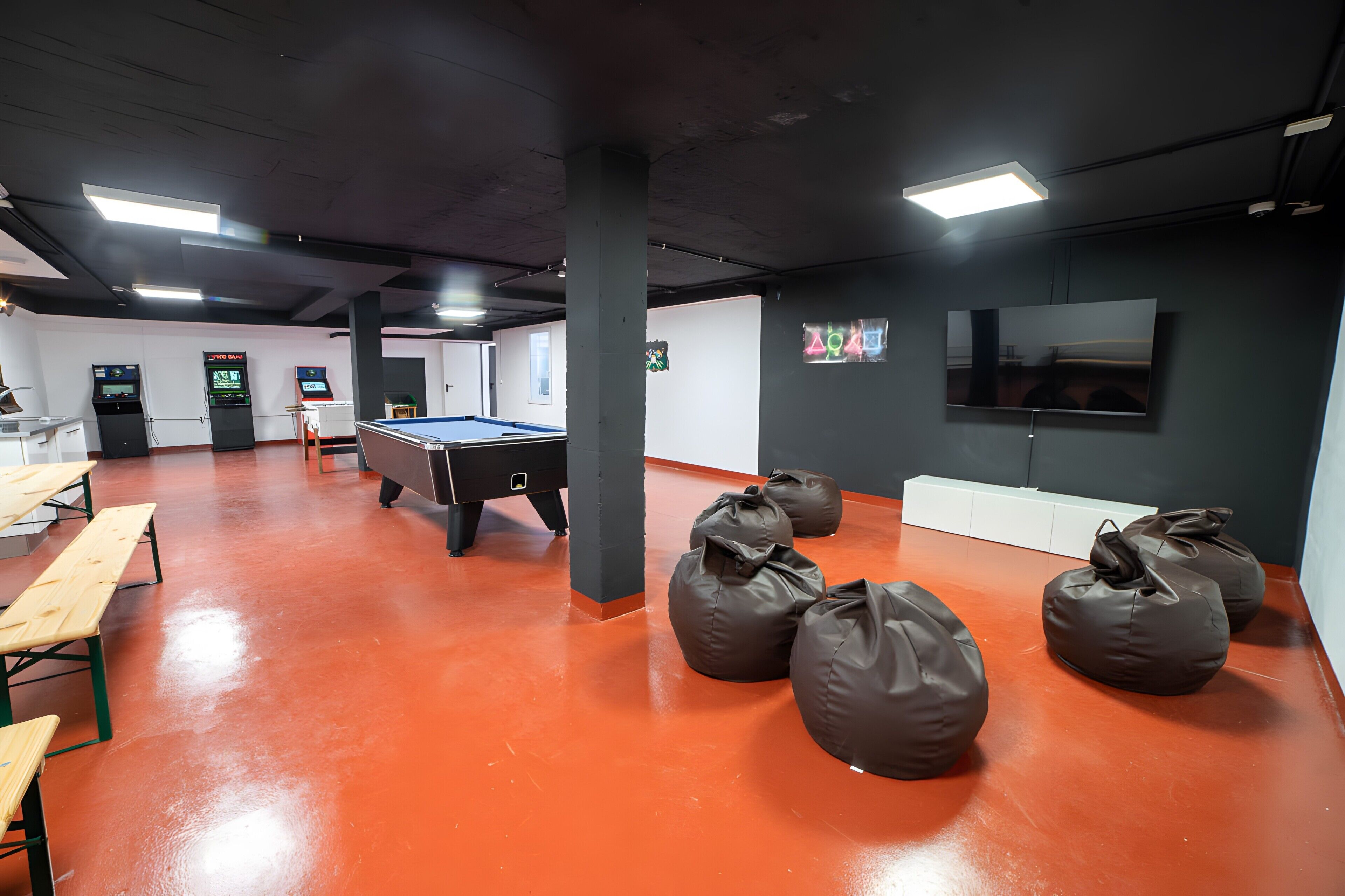 A room with a pool table, bean bags, and a TV mounted on the wall.