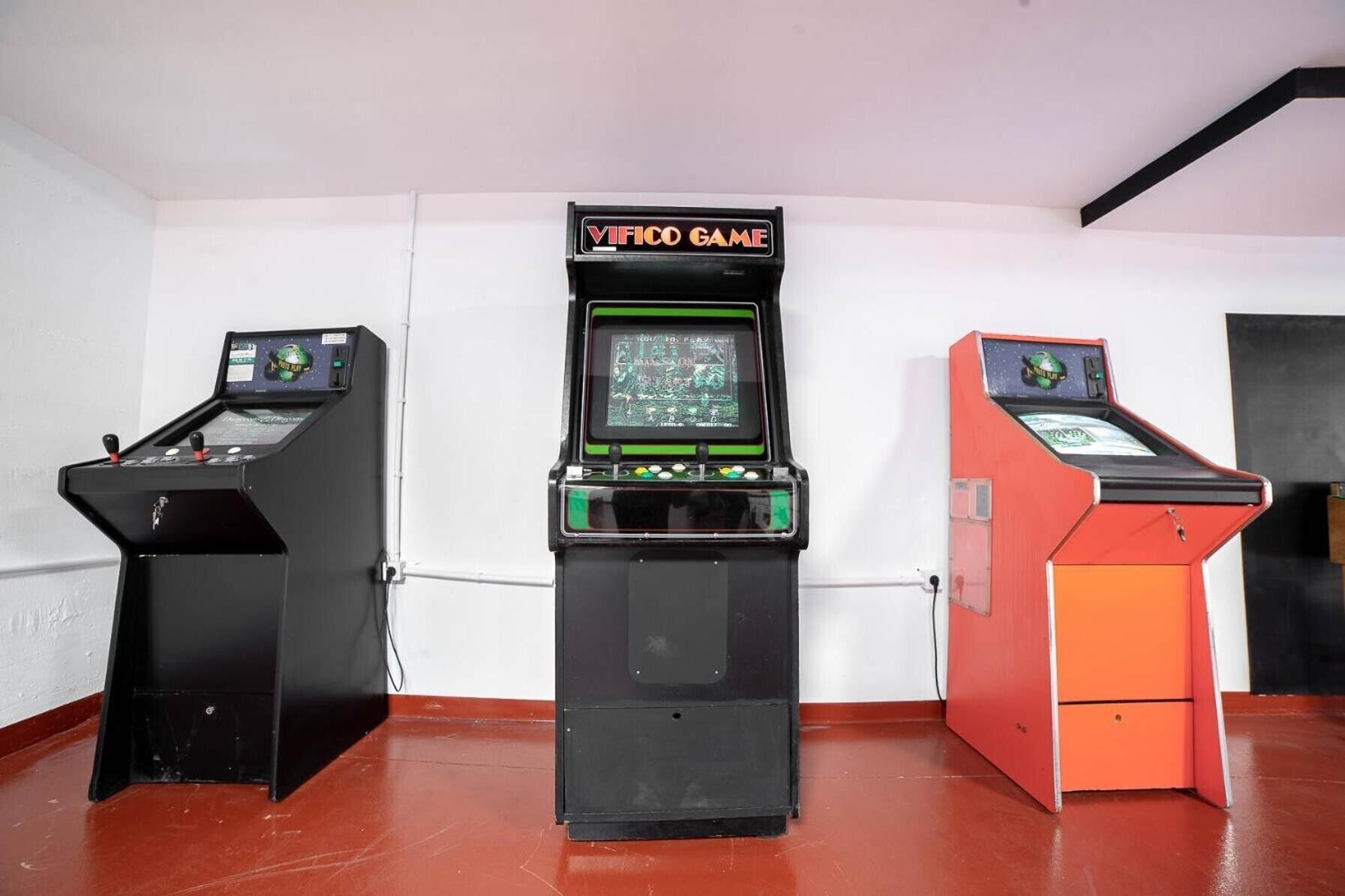Three arcade machines in a room with white walls and a red floor.