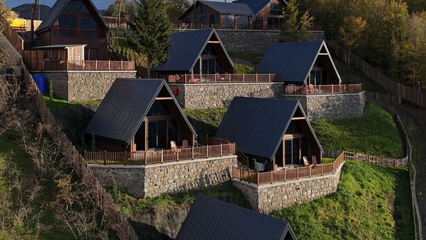 A cluster of mountain cabins with stone foundations and metal roofs, surrounded by lush greenery and trees. - ÖTÜKEN DAĞ EVLERİ (Akçaabat)